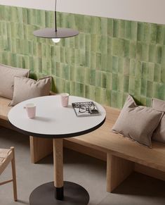 a table with two cups on it in front of a green tiled wall and bench