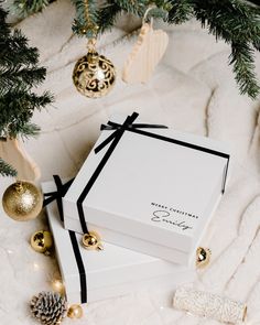 a white box with a black ribbon on it next to christmas decorations and pine cones