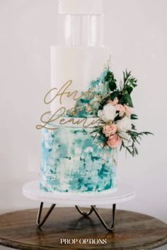 a blue and white wedding cake with flowers on top is sitting on a wooden stand