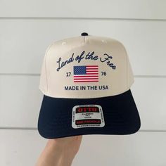 Land of the Free, good 'ole USA. A navy bill trucker hat with adjustable snapback closure, white crown and blue "Land of the Free" text across the front with 1776 detail and american flag graphic. Cotton/ Poly Blend One Size fits most Memorial Day Adjustable Snapback Baseball Cap, Patriotic White Trucker Hat, Patriotic White Snapback Trucker Hat, Patriotic White Snapback Baseball Cap, Patriotic White Trucker Hat/baseball Cap, Patriotic White Snapback Hat, Snapback Hat, One Size, Made In Usa, White Patriotic Snapback Hat, American Style Adjustable Hat For Baseball Season