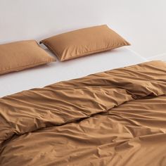 an unmade bed with brown sheets and pillows