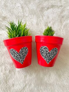 two red flower pots with hearts painted on them sitting on a white furnishing