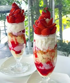 two glasses filled with ice cream and strawberries on top of a white table outdoors