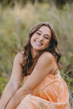 a woman in an orange dress is sitting on the grass and smiling at the camera