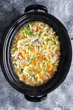 a crock pot filled with chicken noodle soup on top of a gray table