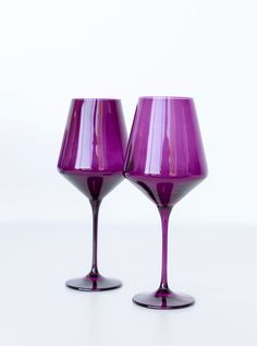 two purple wine glasses sitting next to each other on a white surface with no one around them