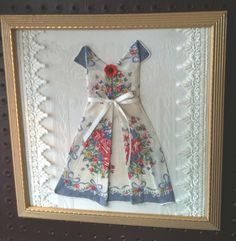 a framed picture with a dress on it's side and a red flower in the center