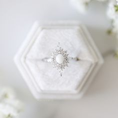 a diamond and pearl ring sitting on top of a white hexagonal box next to flowers