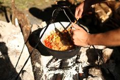 a man is cooking food over an open fire with tongs in his hand,