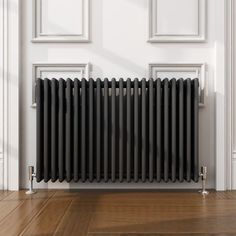 a black radiator is on the floor in front of a white wall and wooden floors