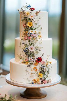 a three tiered white cake with colorful flowers on the top and bottom, sitting on a table