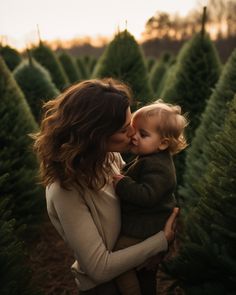 a woman holding a baby in her arms while standing between rows of christmas tree trees