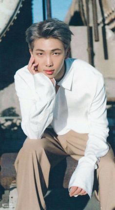 a young man in a white shirt and brown pants sitting on the ground with his hand under his chin