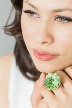 a woman wearing a ring with green flowers on it's middle finger and holding her hand to her face