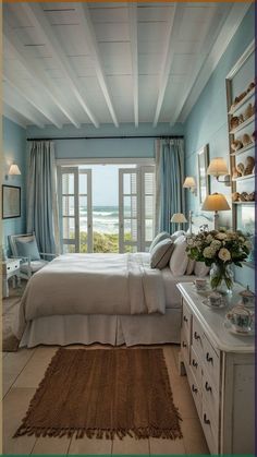 a bedroom with blue walls, white furniture and a large window looking out onto the ocean