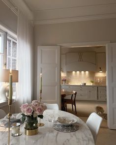 a dining room table with white chairs and flowers on the table in front of it