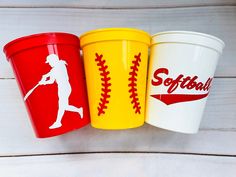 three different colored cups with baseballs and softball logos on them sitting next to each other