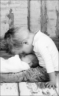 a little boy kissing his baby sister on the cheek while she is holding her head