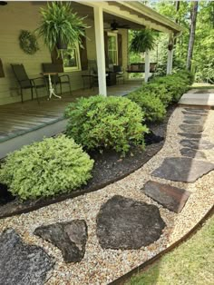 a stone path in front of a house with chairs on the porch and landscaping around it