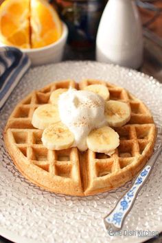 a waffle topped with bananas and whipped cream on a plate next to oranges