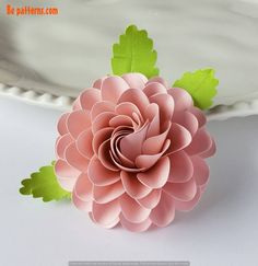 a pink paper flower sitting on top of a white plate with green leaves around it