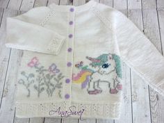 a white knitted sweater with an unicorn and flowers design on the front, sitting on a wooden floor