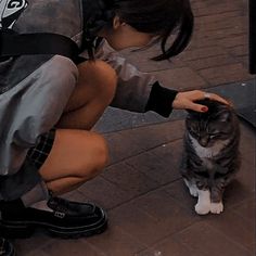 a woman kneeling down petting a cat on the side of a road next to a building