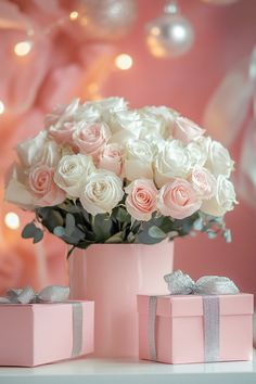 pink and white roses are in a vase next to two small boxes with bows on them