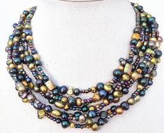 This beautiful 7 strand earthy, beaded necklace is so colorful and unique.  This ooak (one of a kind) statement necklace strung with bronzed gold, greens, blues, copper, and gold freshwater pearls.  It is a statement necklace that will give a fabulous pop of color to any outfit while remaining earthy and boho chic! Substsntial, classy and original, this design is one of my favorites! Perfect for a flowing dress, a work outfit accessory or simply your favorite tank/t-shirt and jeans.  Measurement Unique Multi-strand Necklace With Spacer Beads, Unique Multi-strand Necklaces With Spacer Beads, Bohemian Multi-strand Gold Pearl Necklace, Gold Bohemian Multi-strand Pearl Necklace, Gold Multi-strand Bohemian Pearl Necklace, Work Outfit Accessories, Earth Tone Jewelry, Flowing Dress, Artisan Necklace