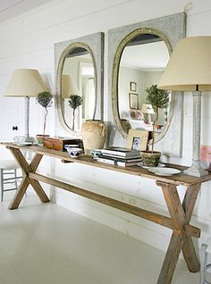 a wooden table topped with two lamps next to mirrors