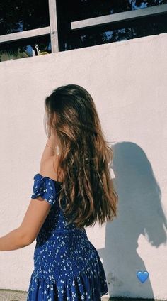 a woman in a blue dress leaning against a white wall with her hand on the ground