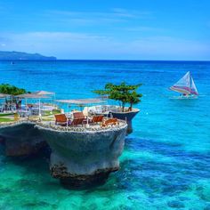 an island in the middle of the ocean with chairs and umbrellas on it's edge