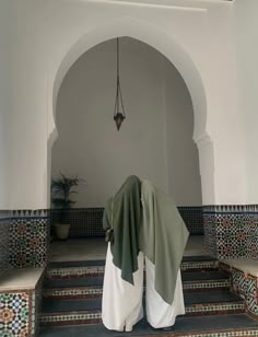 a person with a green shawl standing in front of some stairs and tiled walls