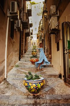 a woman in a blue dress is walking down some stairs with potted plants on either side