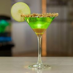 a green cocktail garnished with an apple slice and sprinkled with nuts