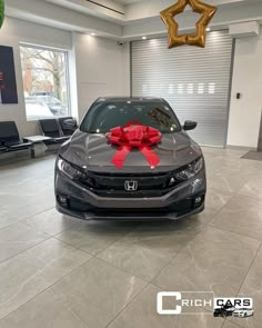 a gray car with a red bow on it's hood in a showroom