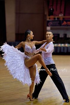 two people are dancing on the dance floor in an arena and one is wearing a white feathered dress