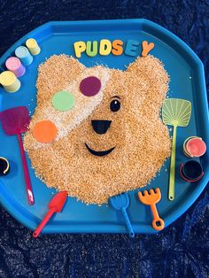 a child's play tray with a bear made out of sand and plastic spoons