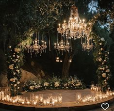 an outdoor ceremony with chandeliers, candles and flowers on the ground at night