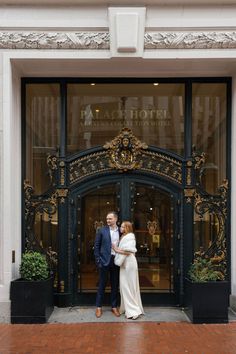 a man and woman standing in front of a hotel entrance with their arms around each other