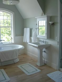 a white bath tub sitting next to a sink under two windows in a bathroom with wooden floors