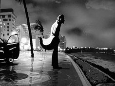 a black and white photo of a person on the street with palm trees in front of buildings