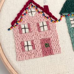 two hand embroidered houses sitting next to each other on a white surface with wooden hoop