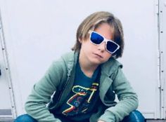 a young boy wearing sunglasses sitting on the ground