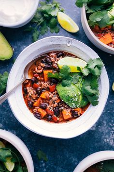 two bowls filled with chili, beans and avocado garnished with cilantro