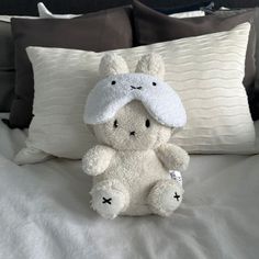 a white teddy bear sitting on top of a bed next to pillows and pillow cases