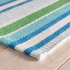 a close up of a rug on a wooden floor with blue, green and white stripes