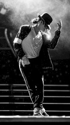 a male in a white shirt and black pants is dancing with his hands up to his face