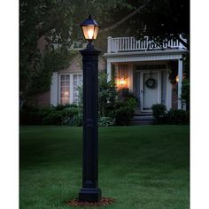 a lamp post in front of a house at night with the lights on and green grass