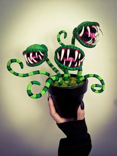 a hand holding a pot with fake green plants in it and two monster heads sticking out of the top